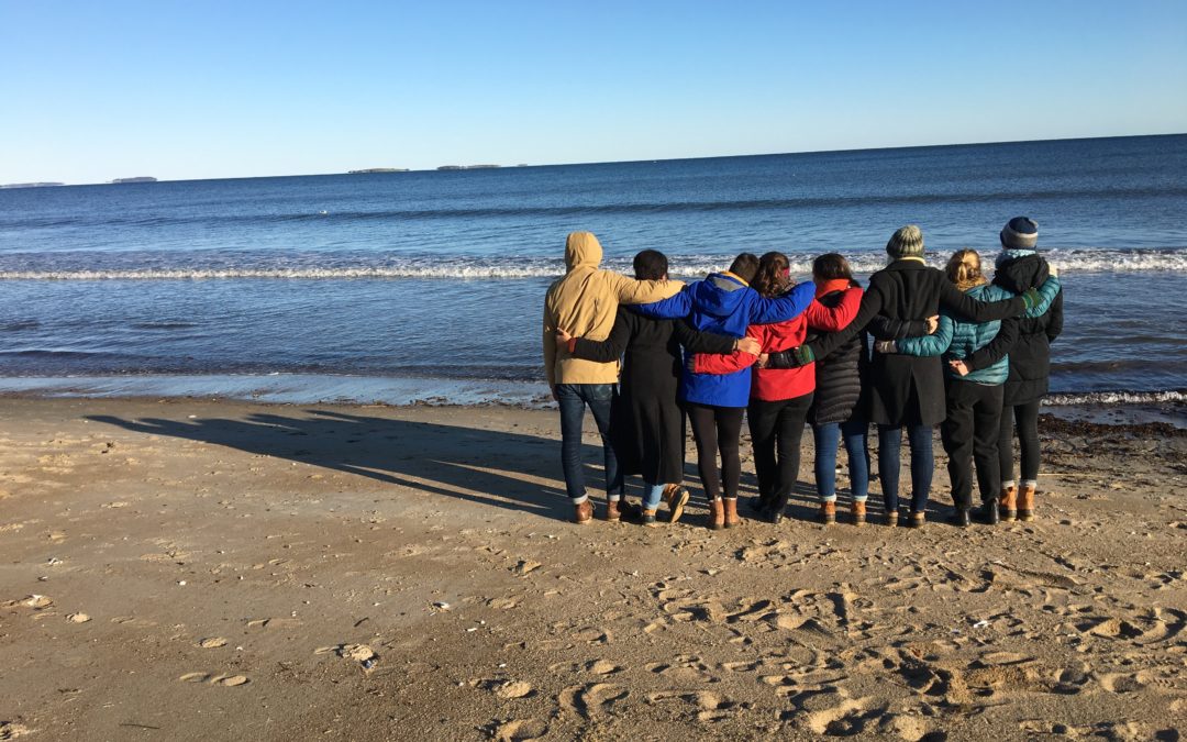 A group of people on the shore looking out to sea with their backs to the camera. In New England.