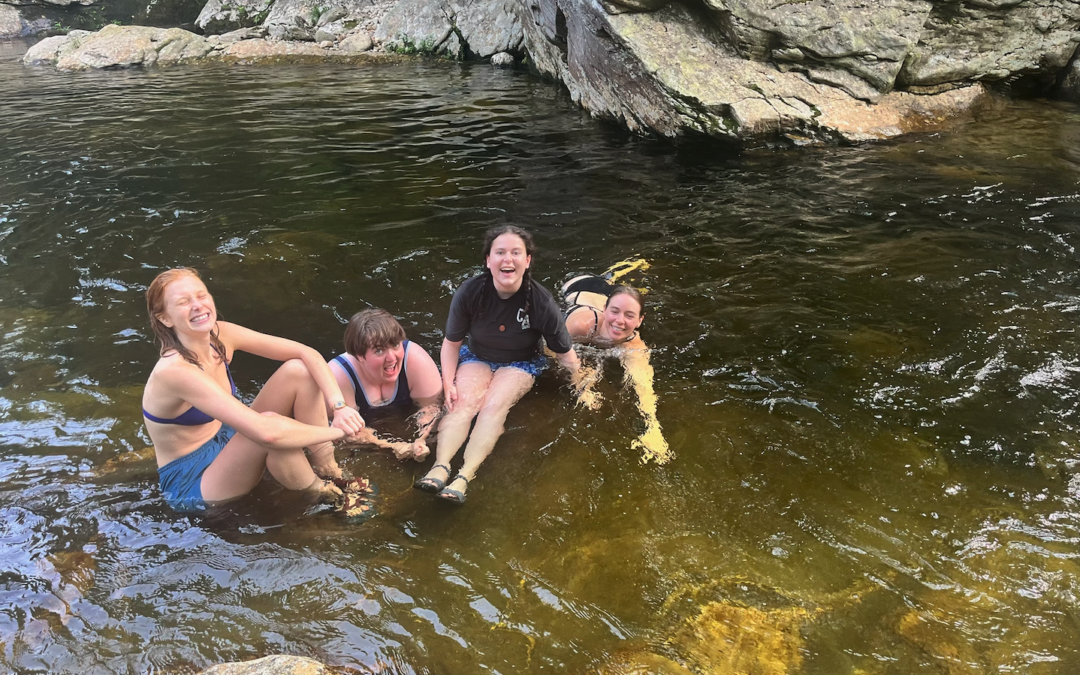 4 people sitting in a rocky river, smiling.